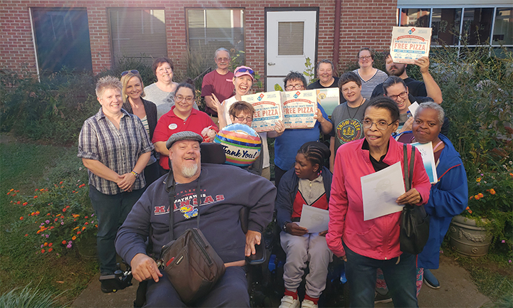 The image shows Kansas BELIEVE team members and self-advocates from a local chapter in Lawrence in 2019. They are celebrating the completion of the Self-Advocate Toolkits and the Sexual Assault Advocacy Toolkits. The image is courtesy of the Kansas BELIEVE team.