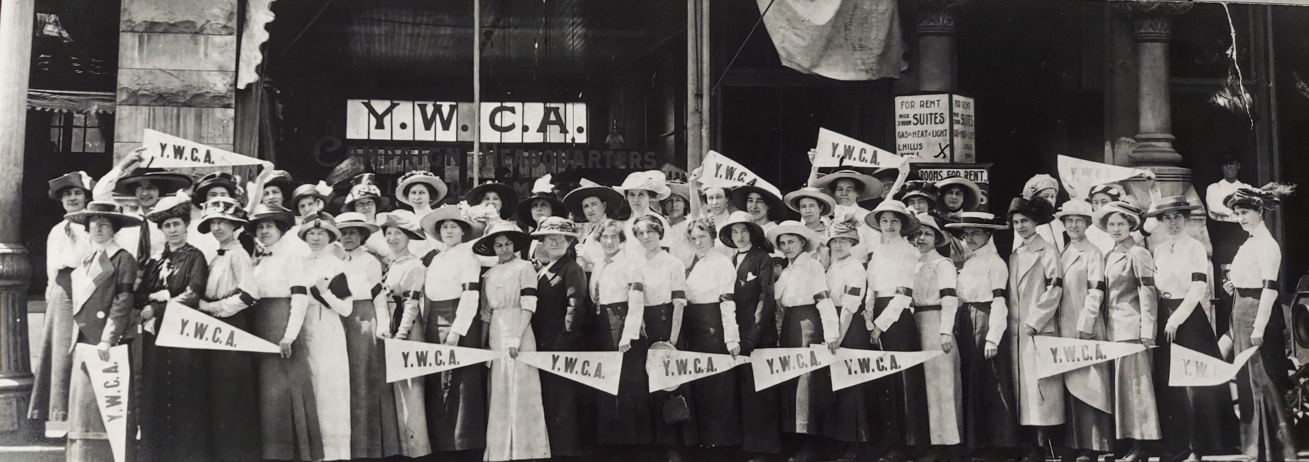 large group of women all wearing dresses and hats standing in front of YWCA building