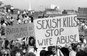 large group of women in the 1970s holding a sign stating sexixm kills stop wife abuse